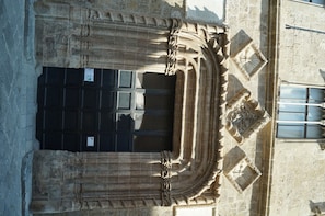 An aerial view of a building with a large, dark entrance, intricate stone carvings, and a window with a grid pattern.