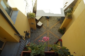 A narrow courtyard with a white umbrella, potted plants, and a stone floor.