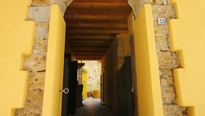 A narrow hallway with a stone archway, wooden ceiling, and yellow walls. - Khalisah (Palermo)
