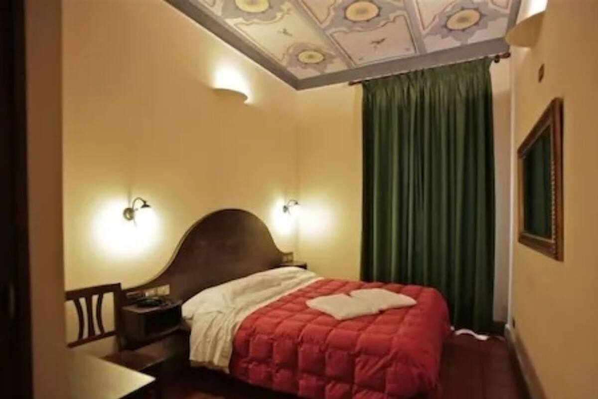 A hotel room with a bed, a nightstand, a chair, and a window with curtains.