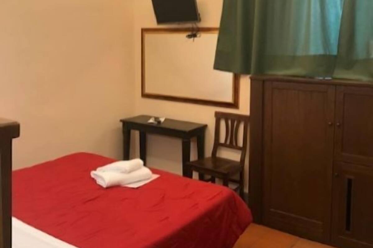A hotel room with a bed, a desk, a chair, a television on a stand, and a wardrobe.