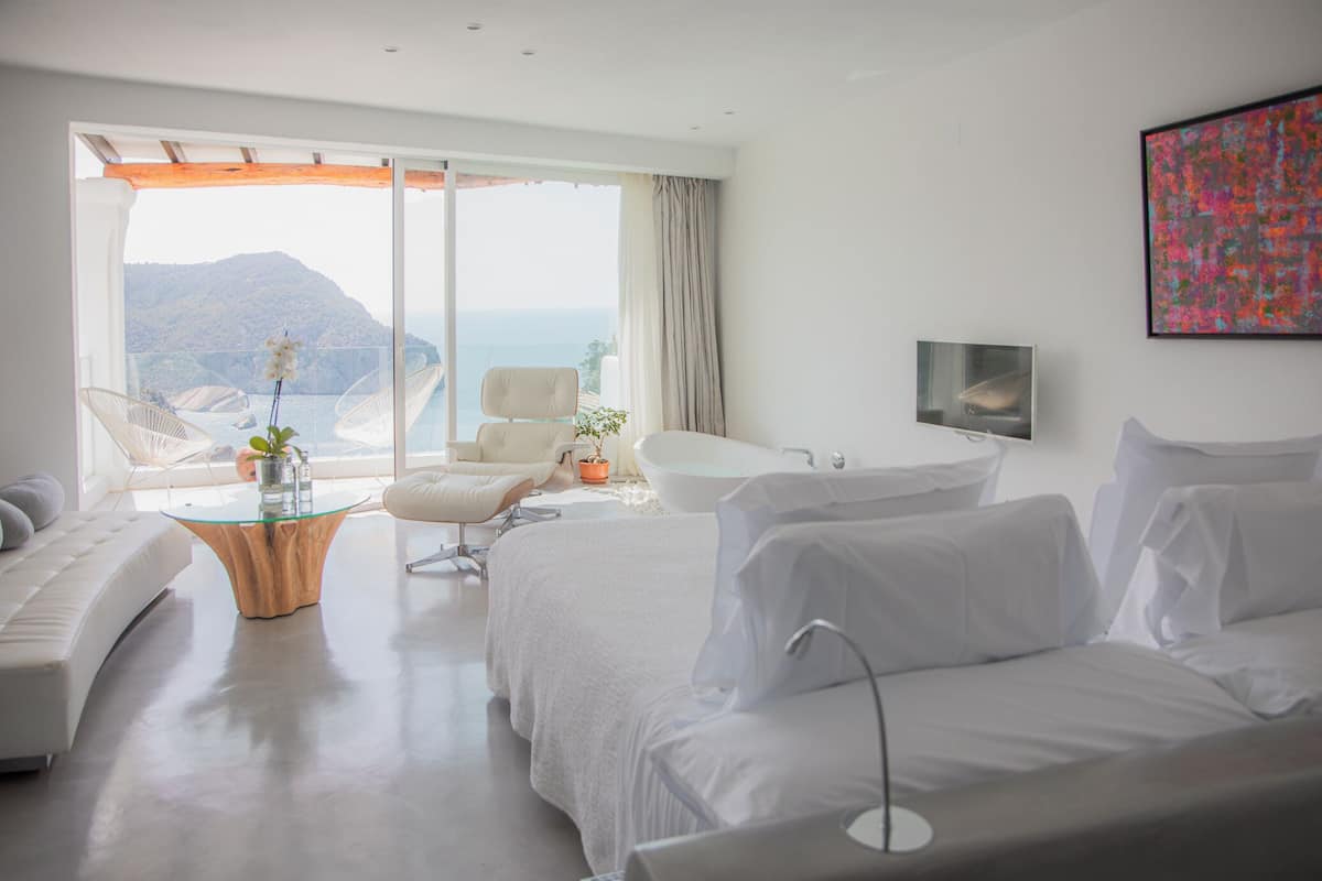 Ein modernes Hotelzimmer mit einem großen Bett, einer Couch, einem Glastisch, einem Sessel und Meerblick.