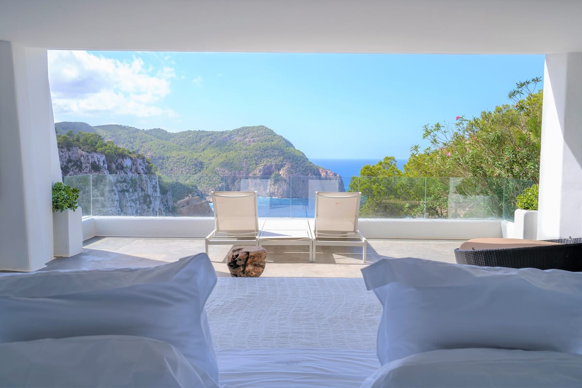 Ein Schlafzimmer mit Blick auf das Meer und die Berge, zwei weiße Stühle und ein großes Fenster.