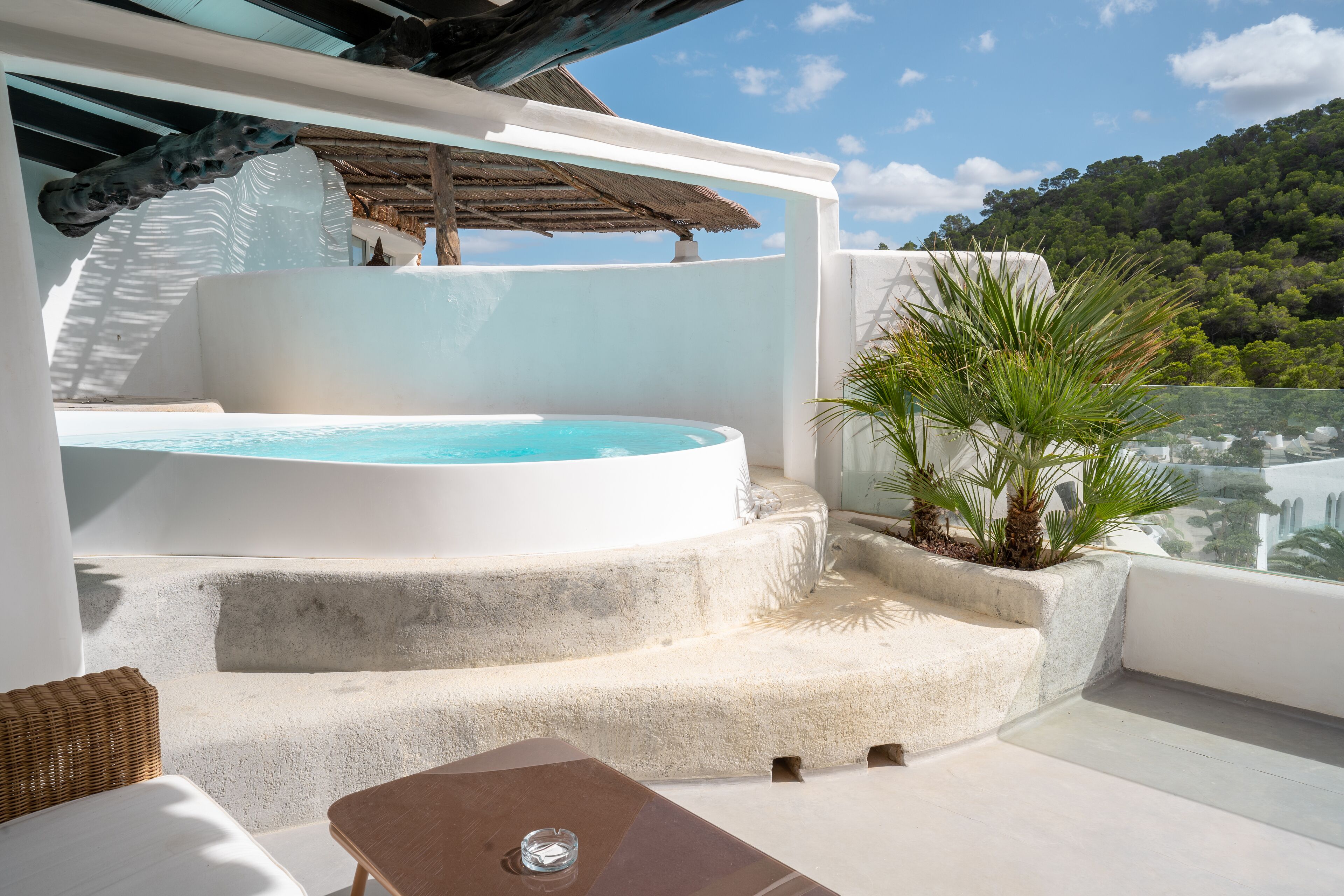 A rooftop terrace with a hot tub, outdoor seating, and a view of a lush hillside.