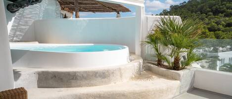 A rooftop terrace with a hot tub, outdoor seating, and a view of a lush hillside.