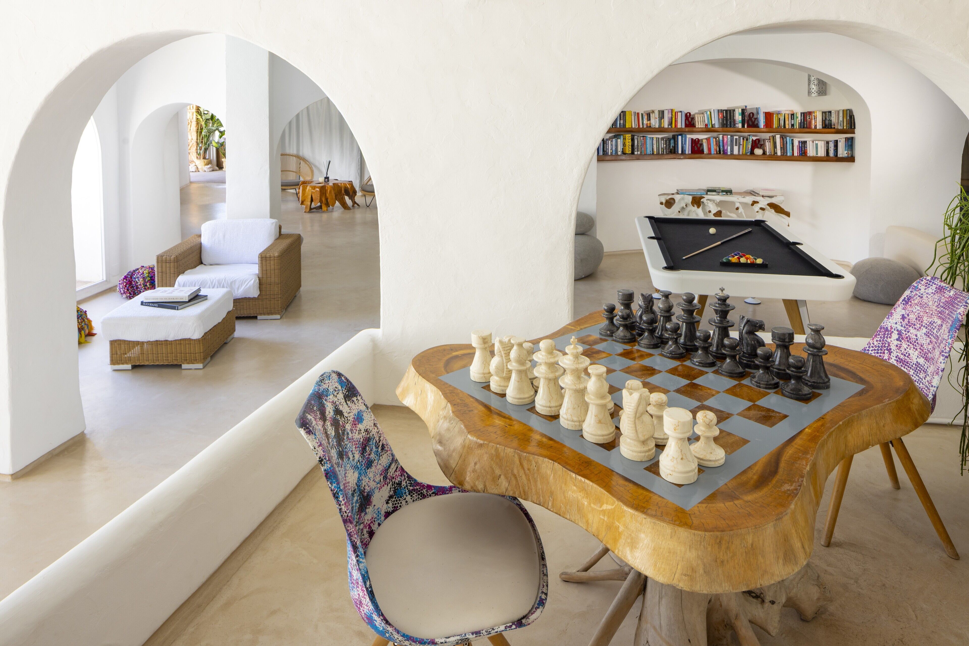 A cozy living room with a wooden chess table, comfortable seating, and a bookshelf filled with books.