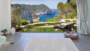 Un dormitorio con una cama grande, vista al mar, pared de piedra y jardín.