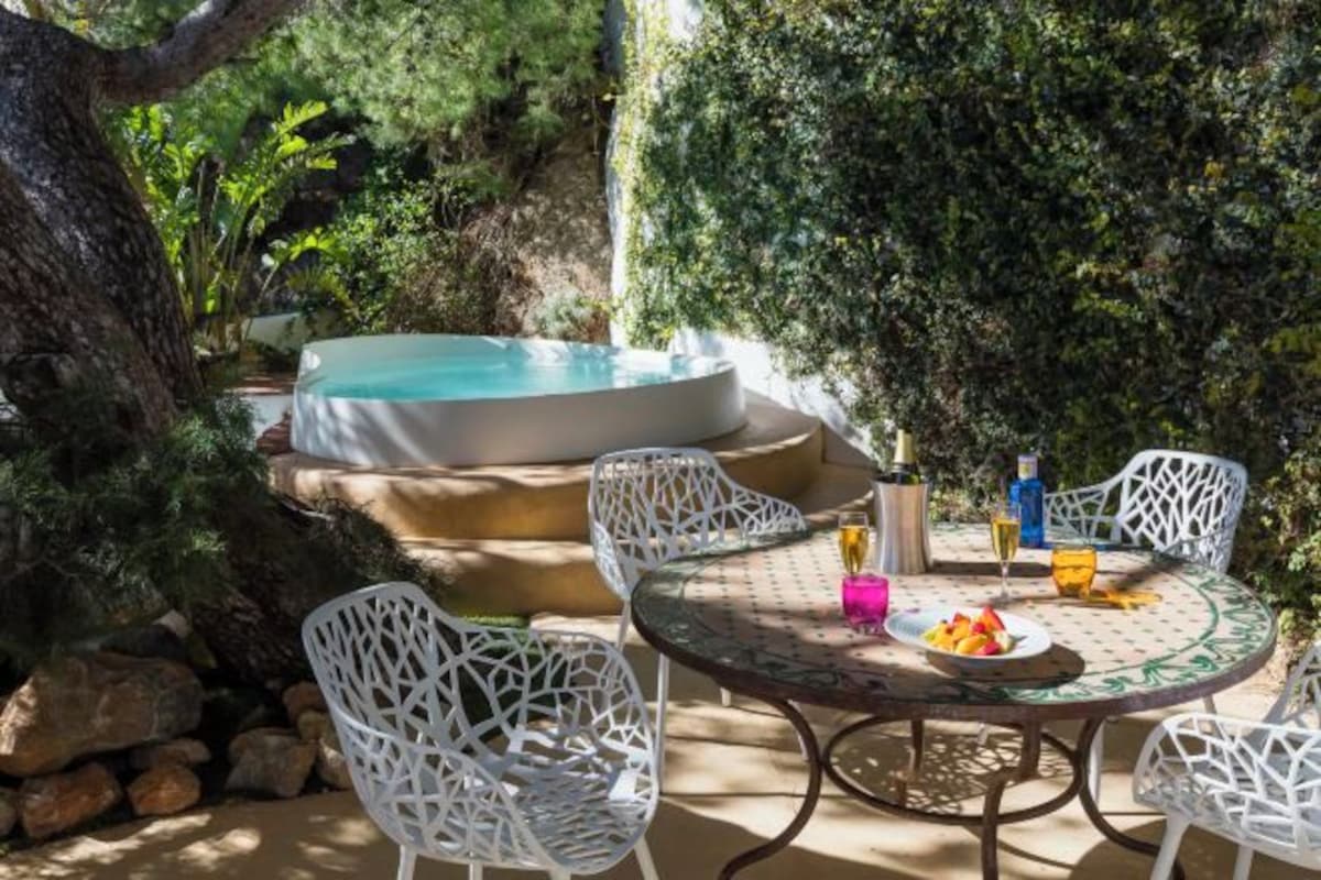 Een ronde tafel met witte stoelen, een jacuzzi en een stenen muur.