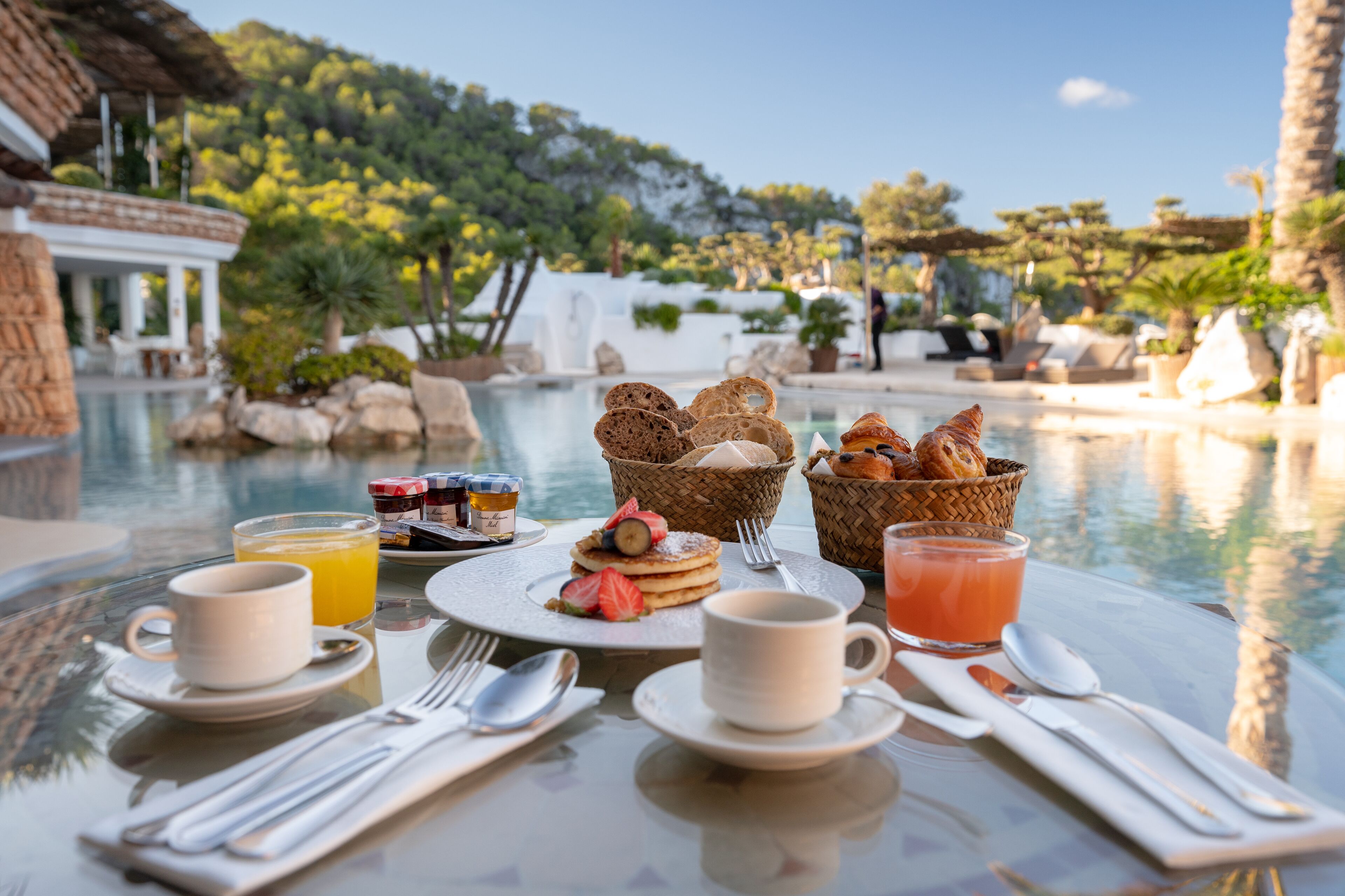 A breakfast setup by a pool with a view of a building and trees.