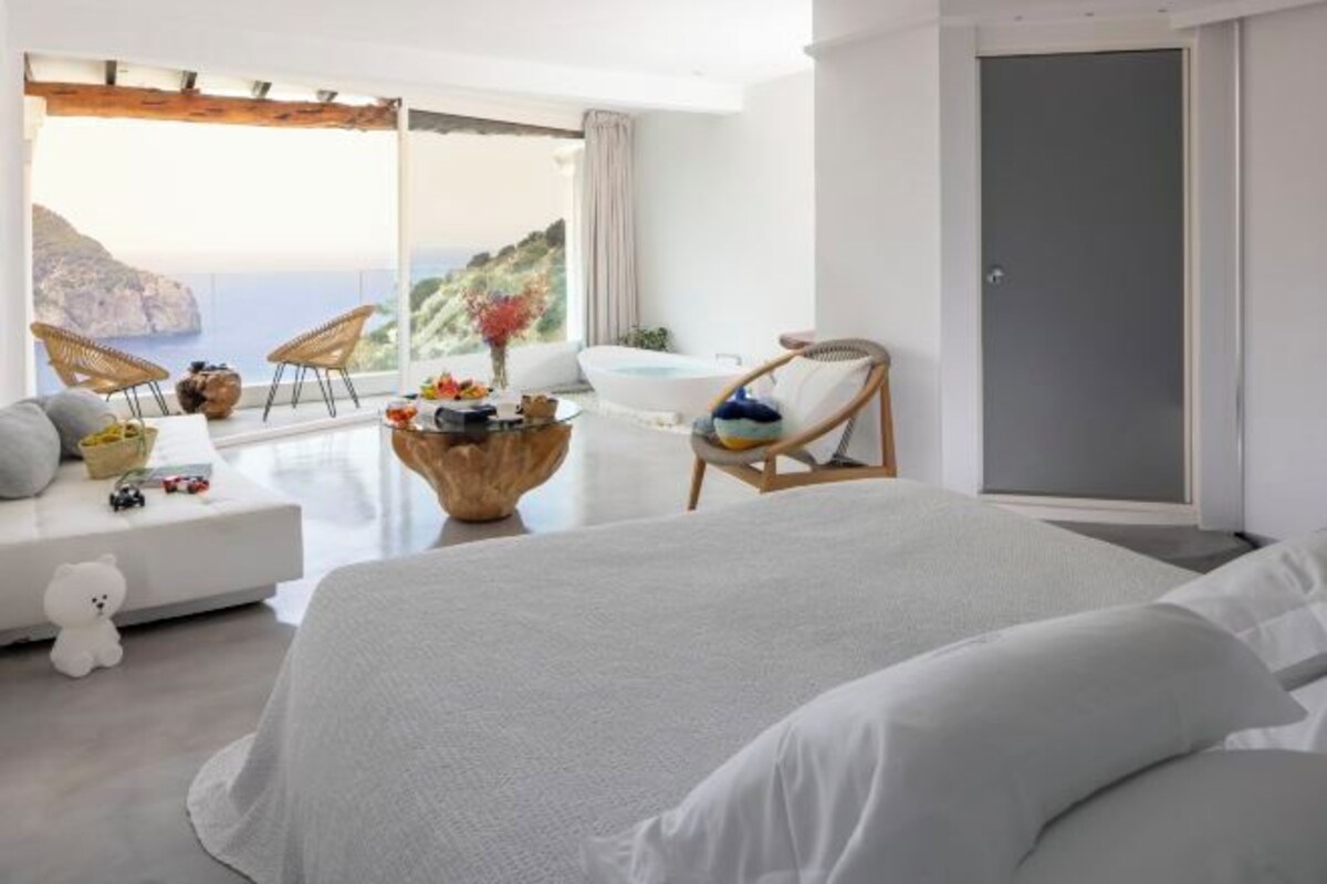 Een slaapkamer met een groot bed, een bank, rieten stoelen, een kleine tafel en uitzicht op zee.