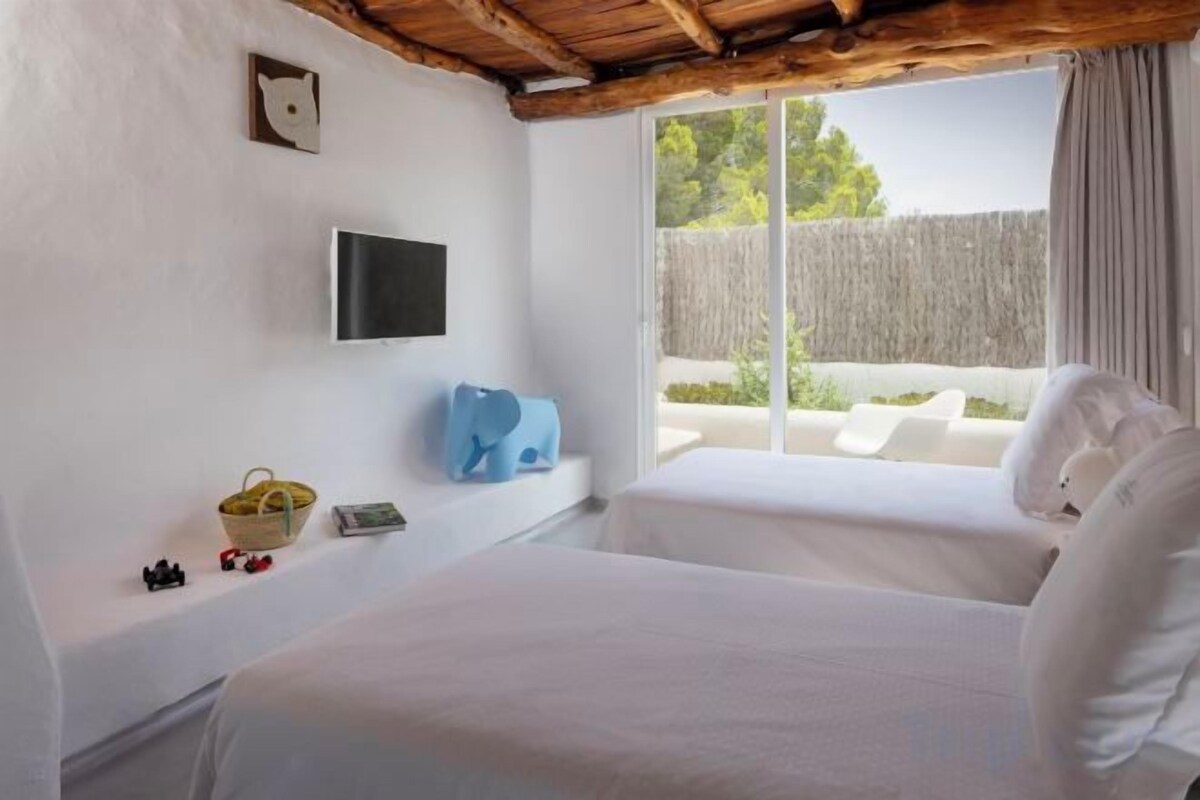 A bedroom with a bed, a television, a window with a view of the outside, and a small shelf with items.