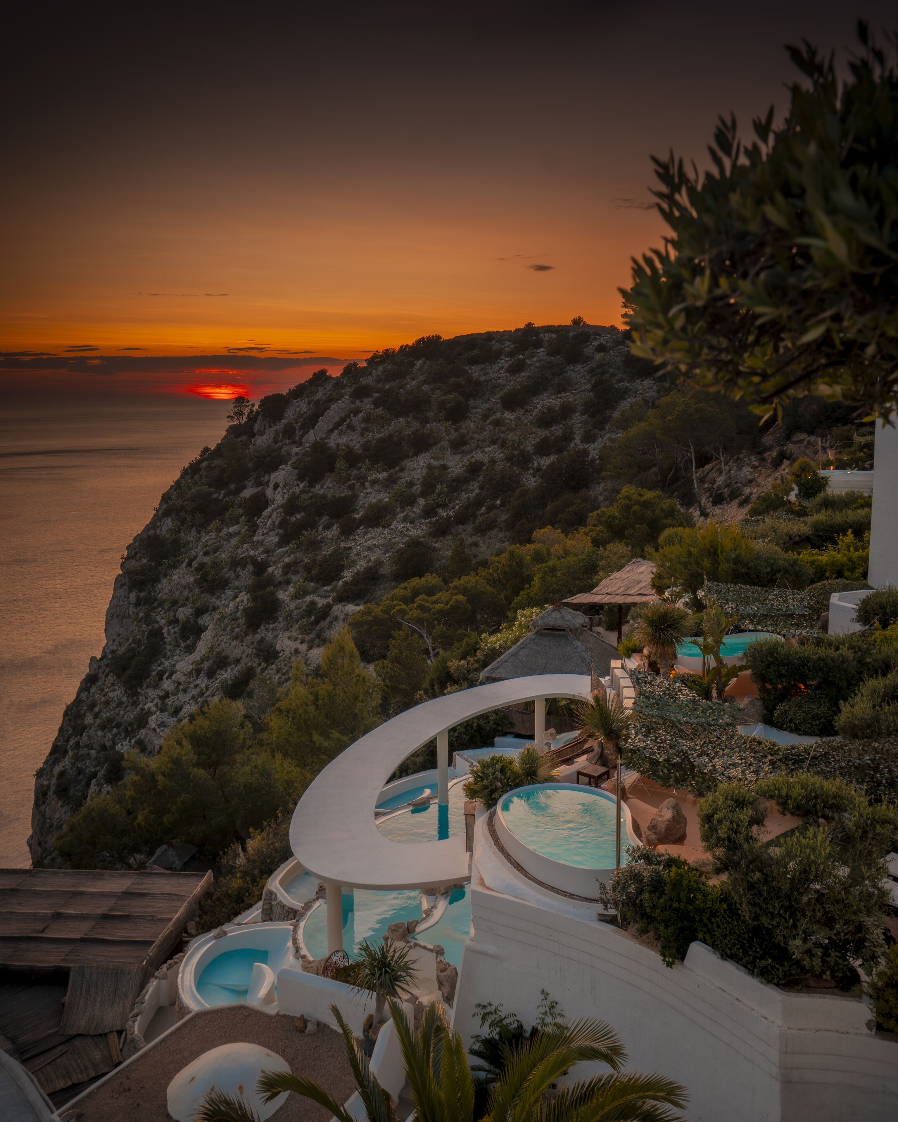 Um resort com área de piscina, vista para o mar e paisagem montanhosa ao fundo.