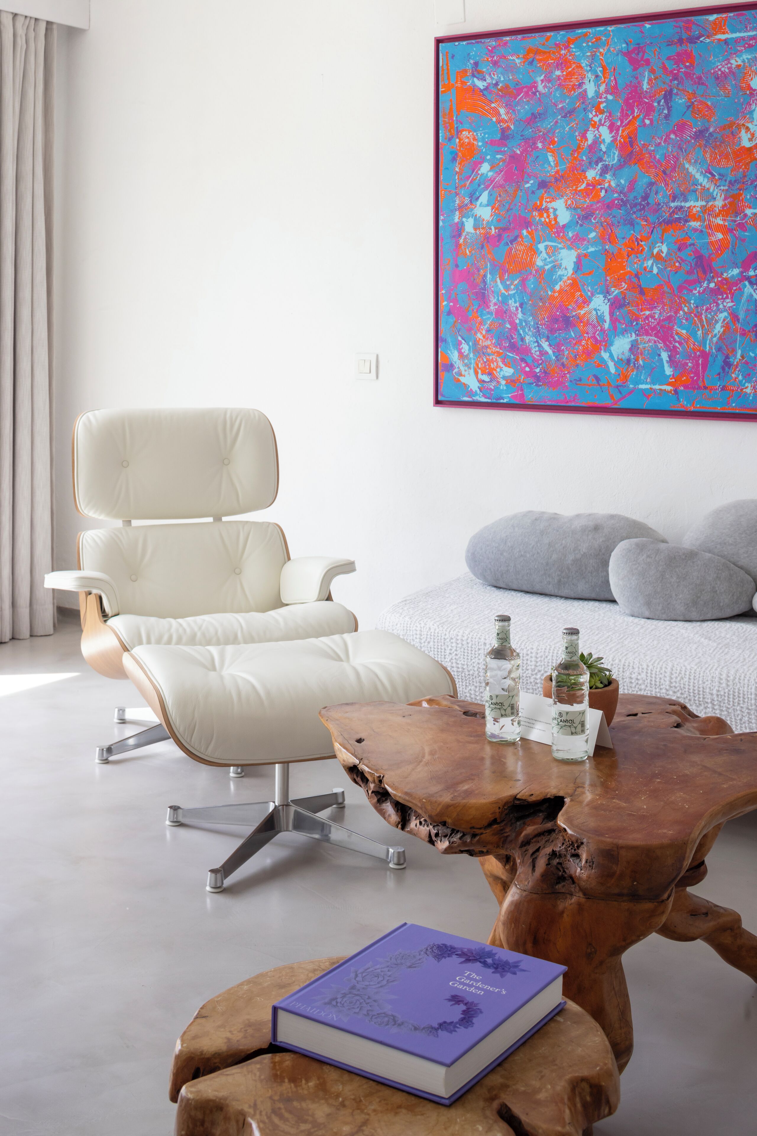Un moderno salón con un sillón de cuero blanco, una mesa de centro de madera con un libro y un gran cuadro abstracto en la pared.
