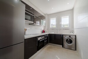 A modern kitchen with stainless steel appliances, a built-in oven, and a washing machine.