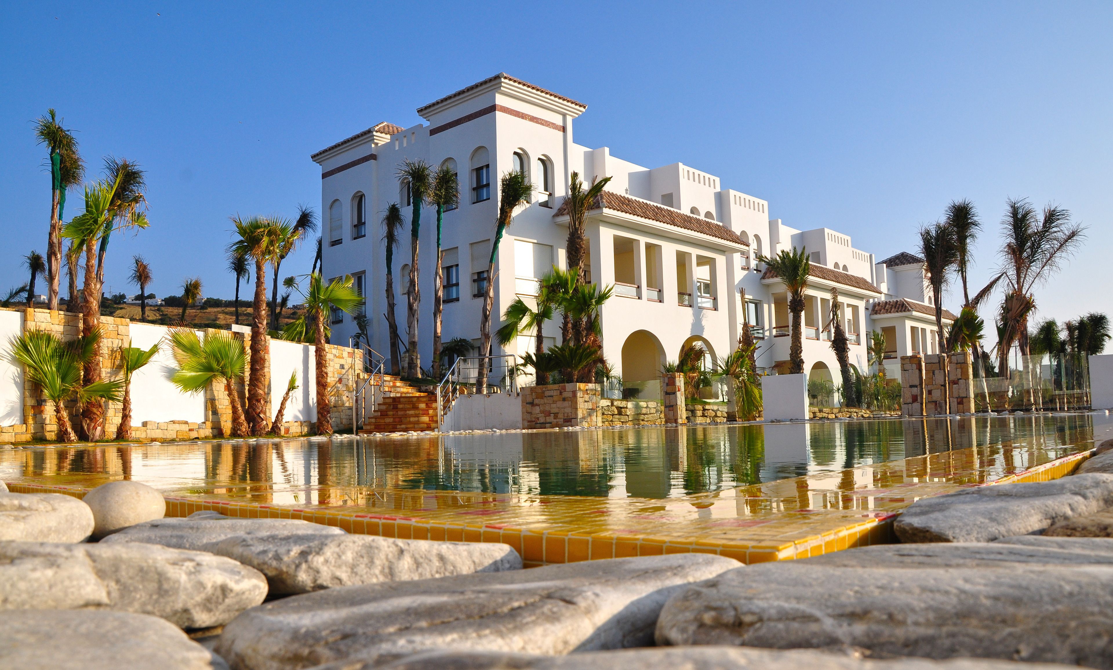A large white building with multiple balconies and a swimming pool in the foreground.