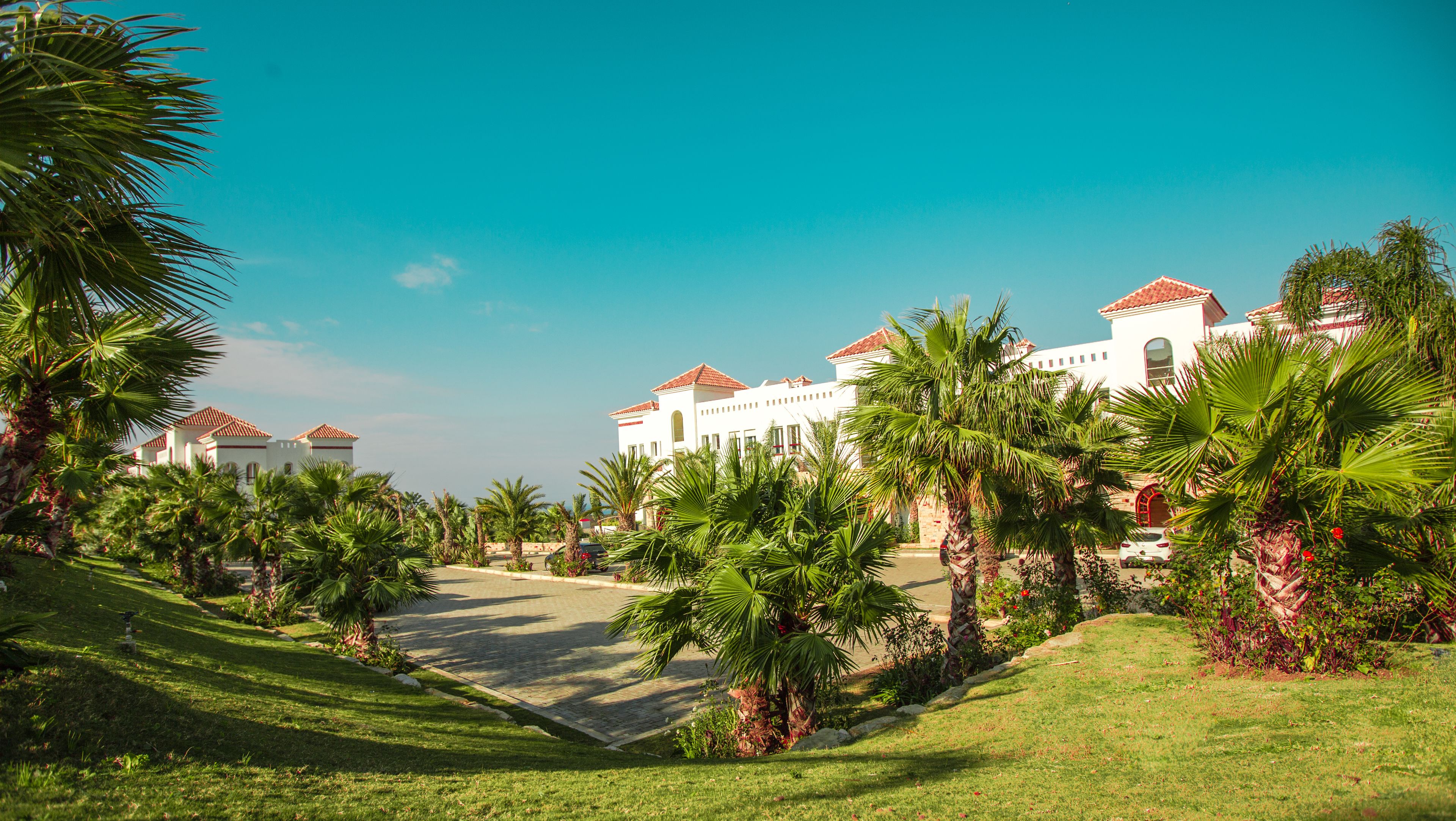 A large, white building with red-tiled roofs, surrounded by well-maintained lawns and palm trees.