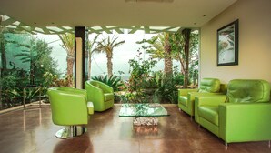 Una sala moderna con sofás de cuero verde, una mesa de centro de vidrio y vistas a plantas tropicales y palmeras a través de amplios ventanales.