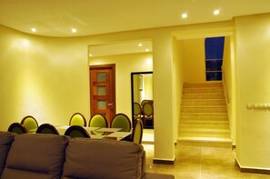 A living room with a sofa, a dining table with chairs, a staircase, and a door leading to another room.