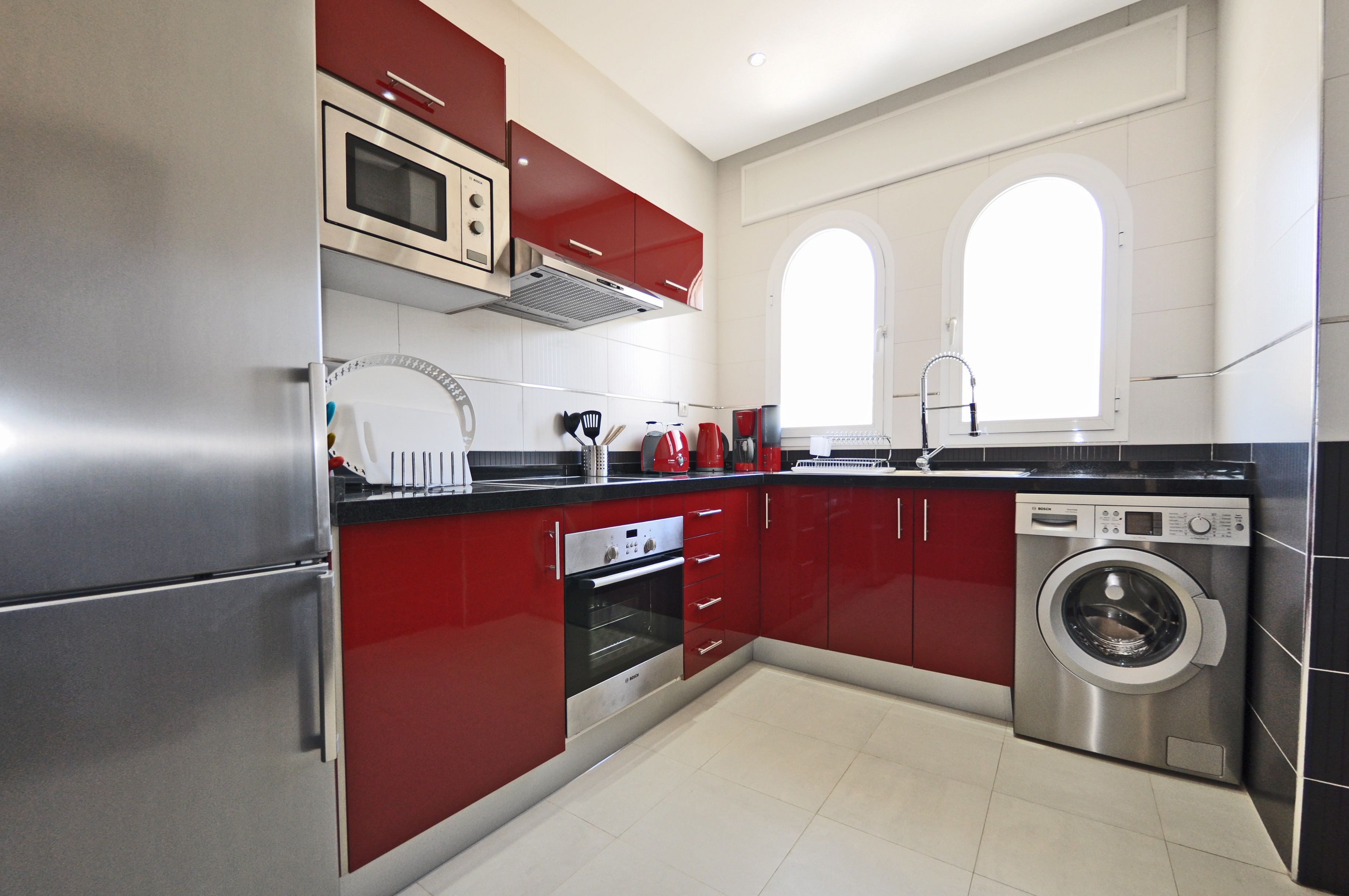 Una cocina moderna con electrodomésticos de acero inoxidable, muebles de color rojo y lavadora incorporada.