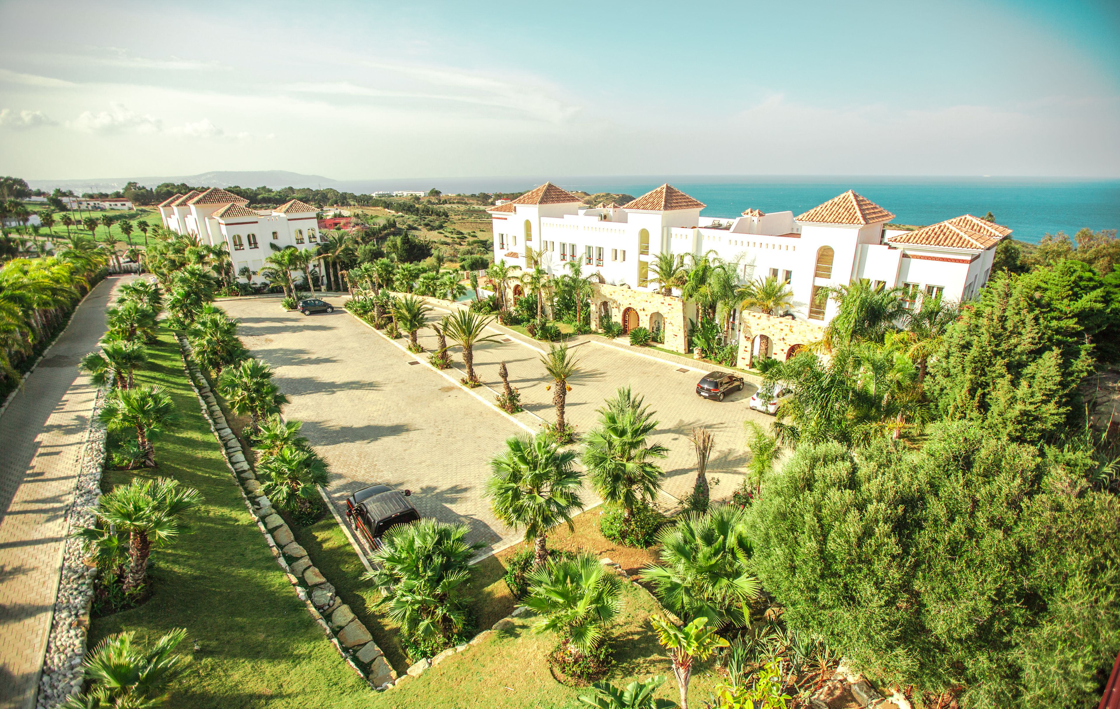 A resort with multiple white buildings, a paved driveway, and palm trees.