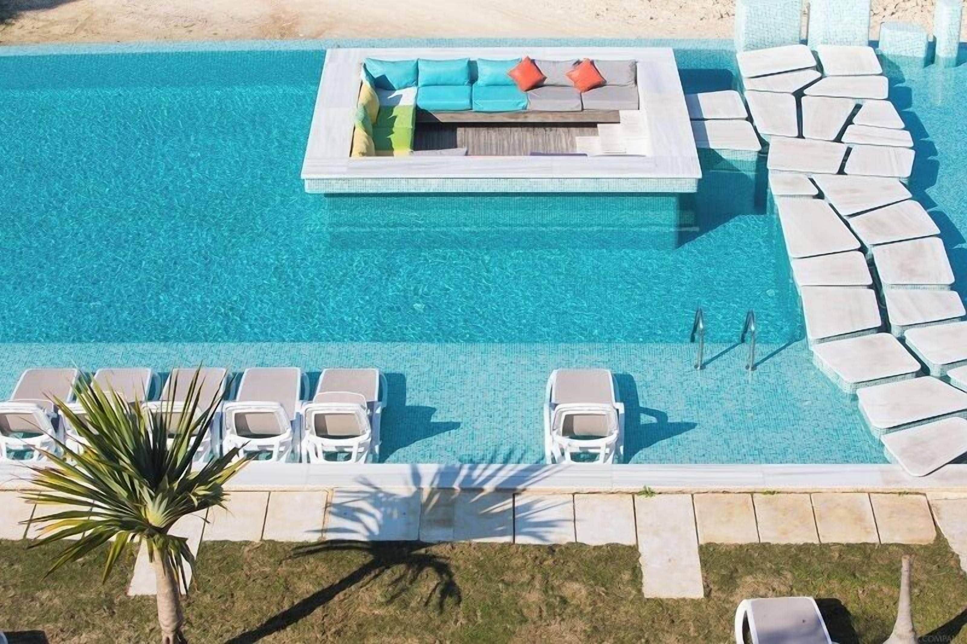 Vista aérea de una piscina con sillas de descanso y una zona para tomar el sol.