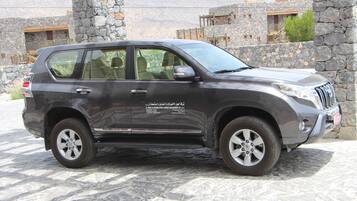 Un SUV grigio parcheggiato di fronte a un edificio in pietra con un cartello.