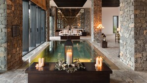 Un área de piscina interior lujosa con paredes de piedra, un banco de madera y velas.