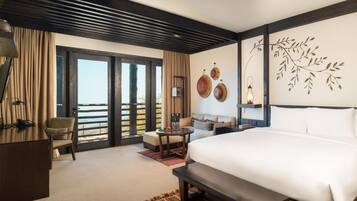 A hotel room with a large bed, a desk, a sofa, and a balcony with a view.
