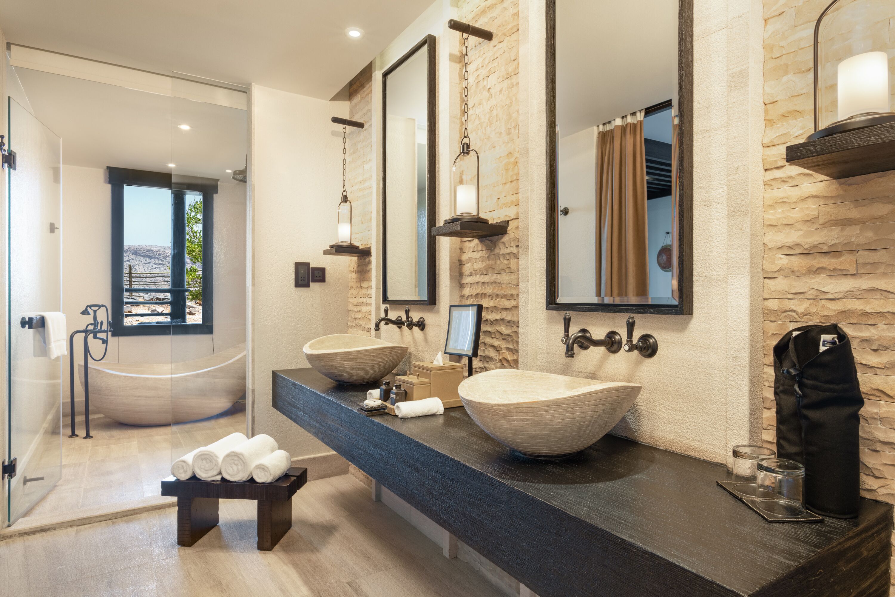 A modern bathroom with two large vessel sinks, a glass-enclosed shower, and a view of the outdoors.