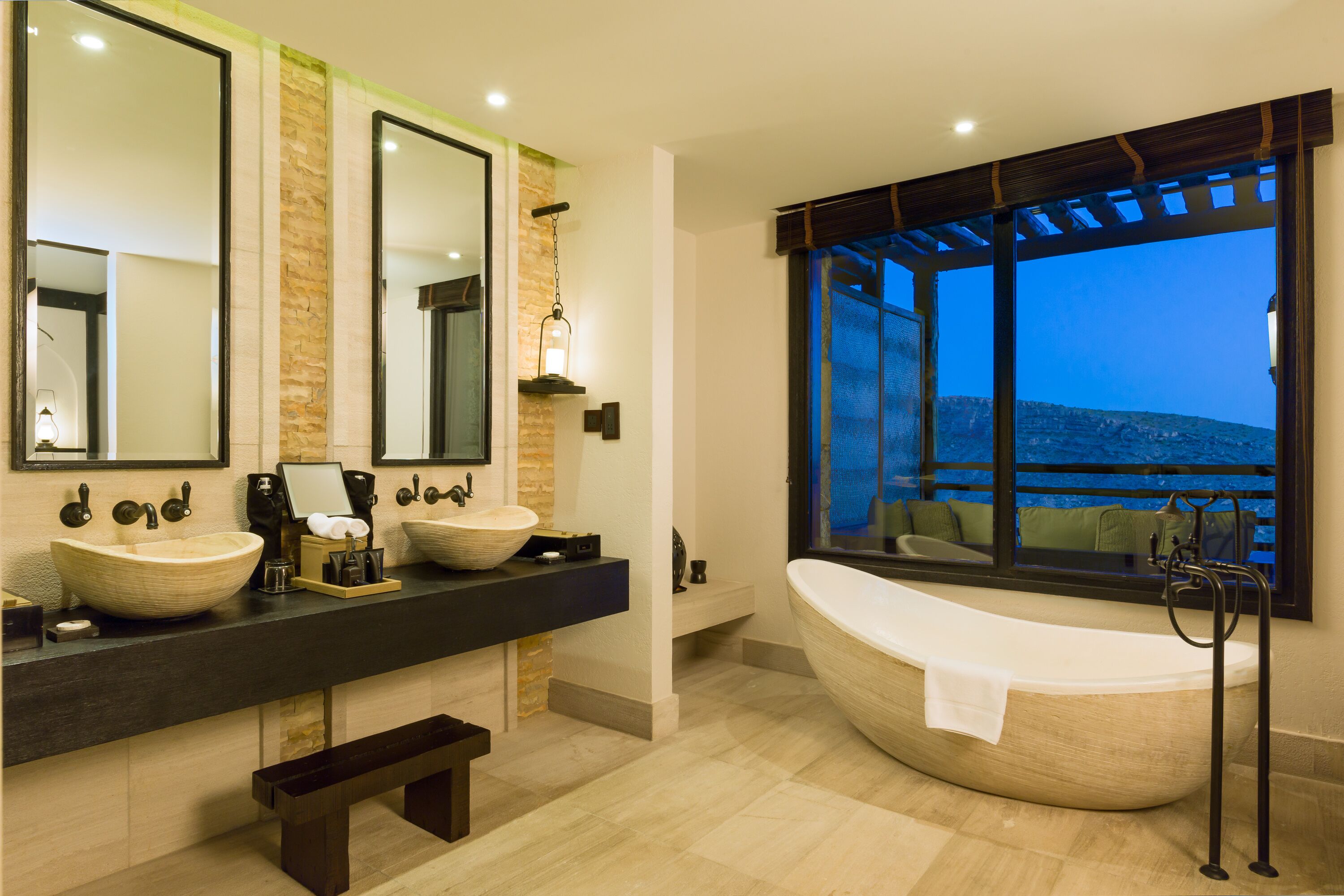 A modern bathroom with a large freestanding bathtub, two sinks with large mirrors, and a view of the outdoors through a large window.