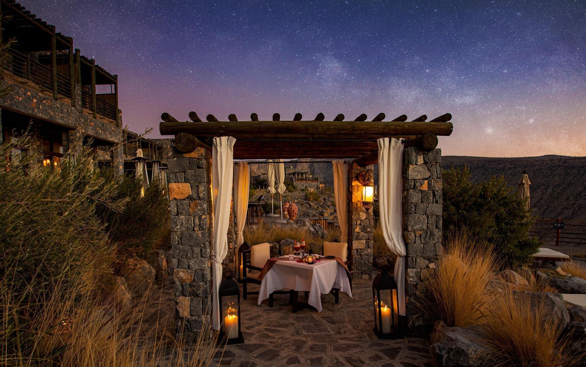 An outdoor dining area with stone walls, a pergola, and a starry night sky.