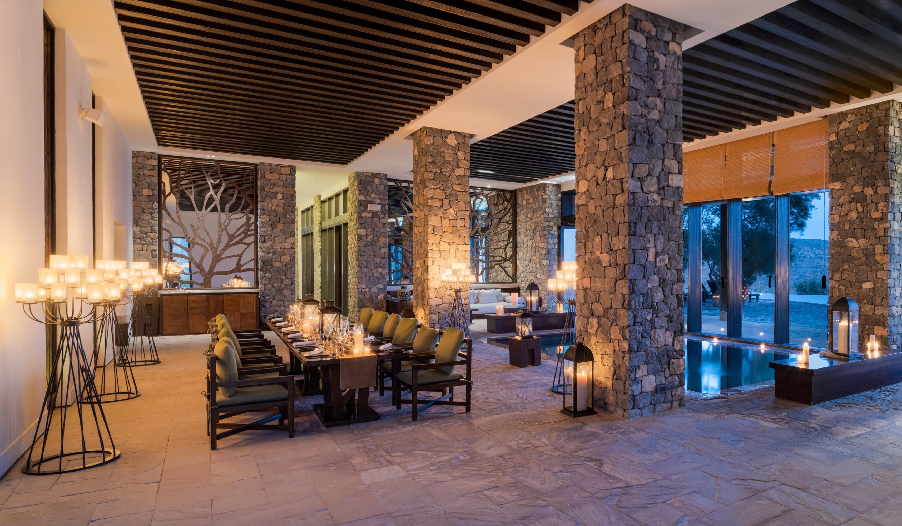 A spacious outdoor dining area with stone pillars, a pool, and a view of the landscape.