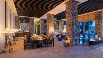 A spacious outdoor dining area with stone pillars, a pool, and a view of the landscape.