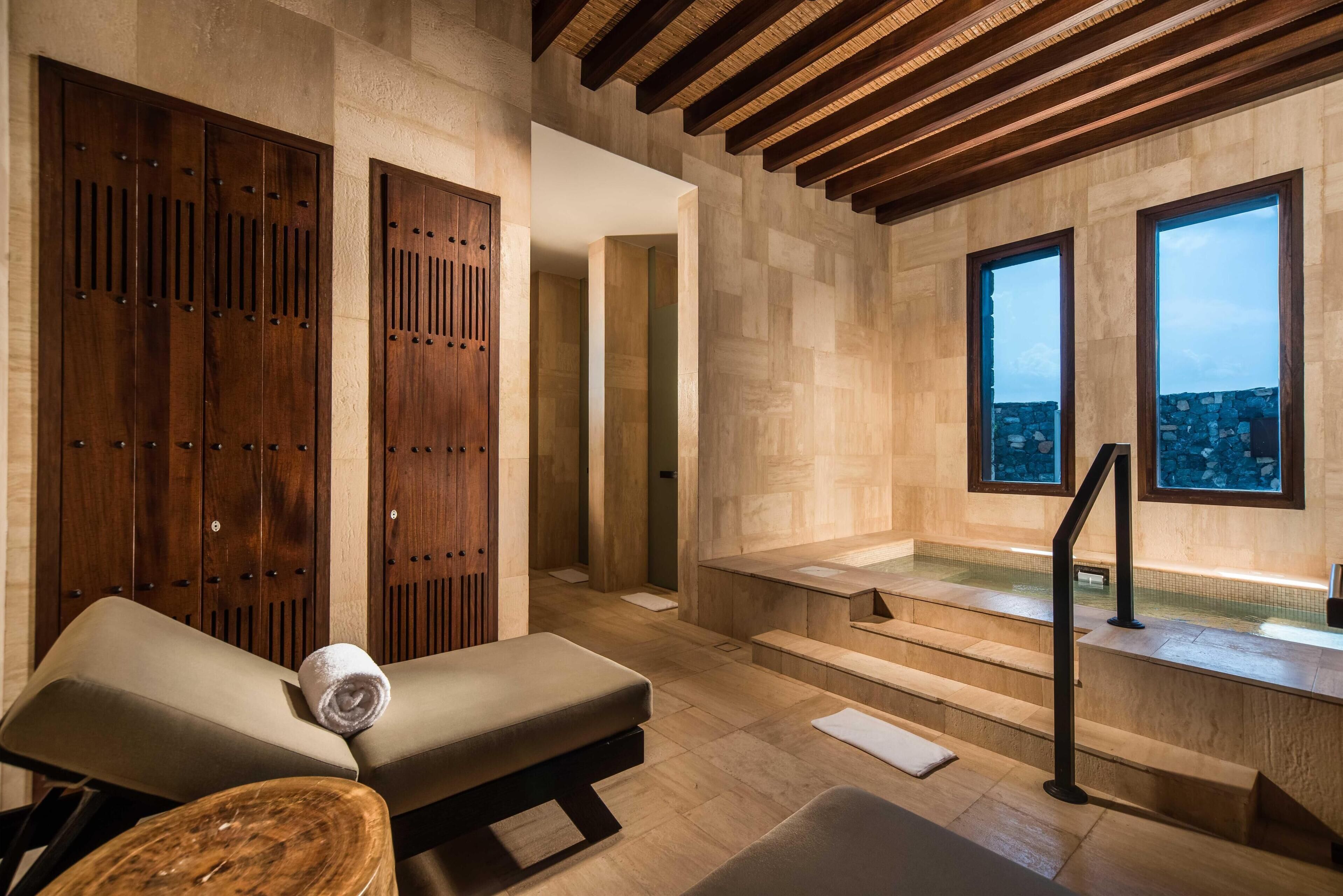 A spa area with wooden lockers, a massage table, and a view of the city through large windows.