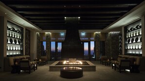 A lobby with a central fire feature, stone walls, and shelves with decorative items. - Alila Jabal Akhdar, Oman (Nizwa)