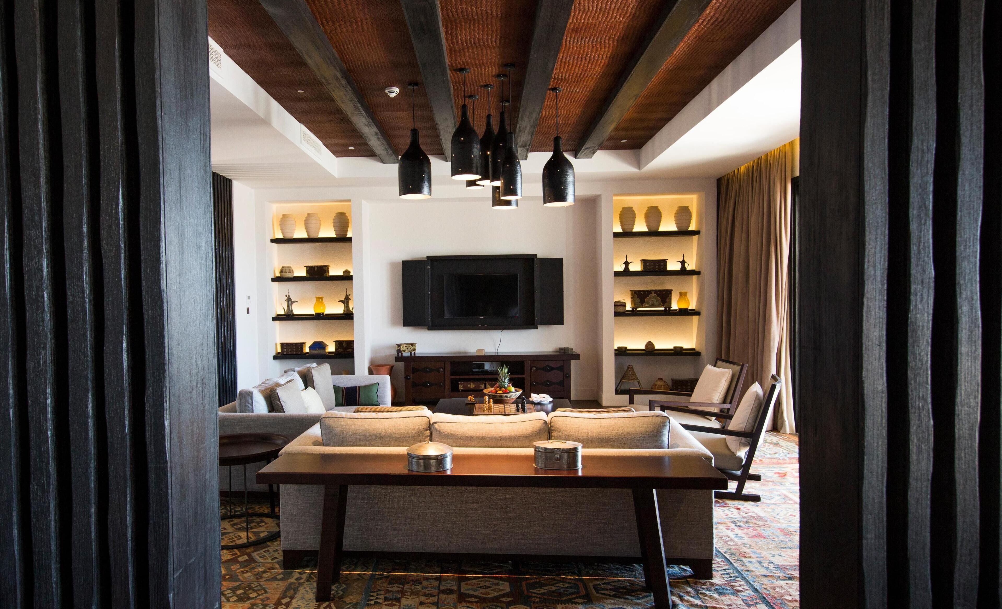 A modern living room with a sofa, coffee table, and TV. There are shelves with decorative items and a patterned rug.