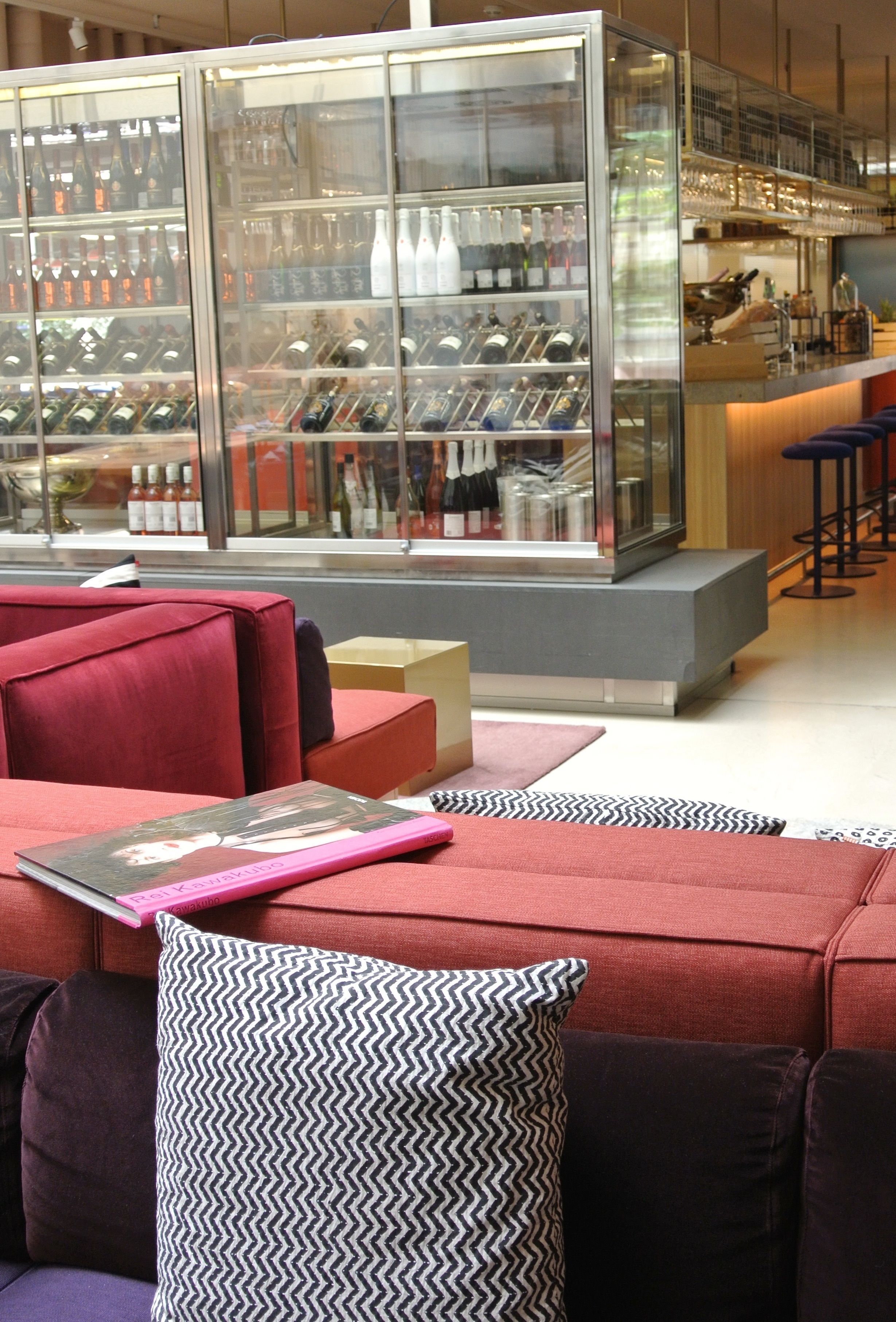 A modern bar area with a glass display case of bottles, red seating, and a bar counter.