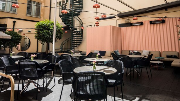 Un'area salotto esterna con tavoli e sedie, una scala a chiocciola e un soffitto in vetro.