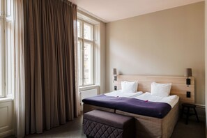 A hotel room with a large bed, a bedside table, a nightstand, a window with curtains, and a radiator. - Scandic No 53 (Stockholm)