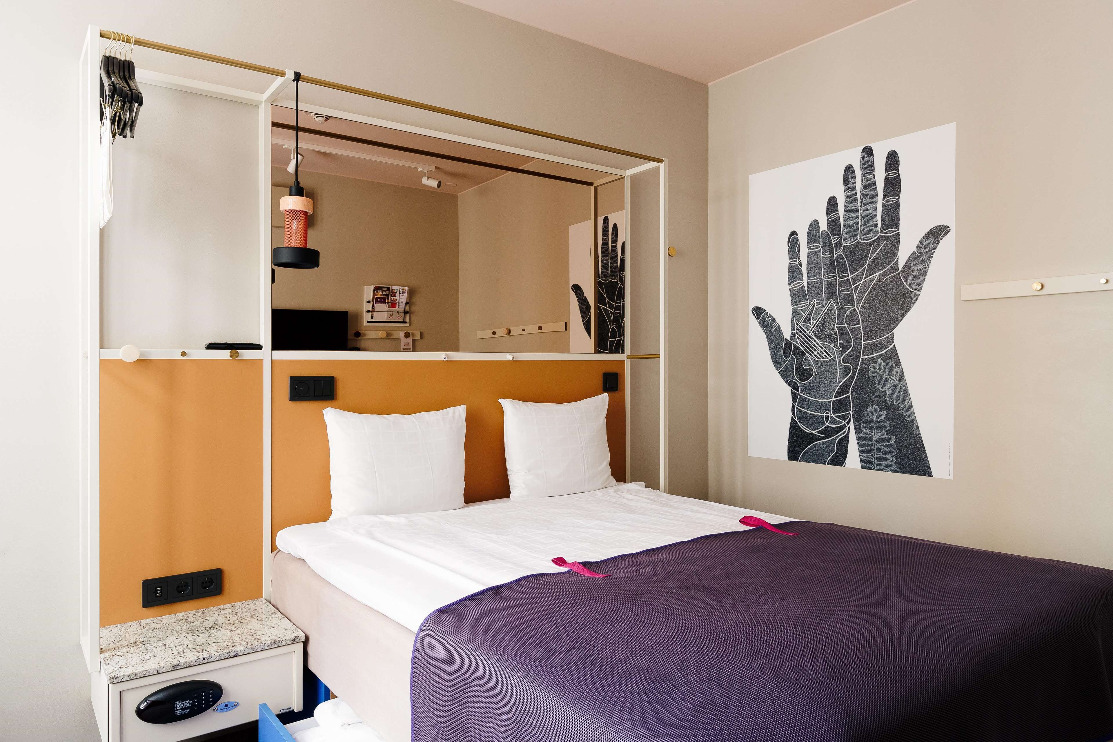 Una habitación de hotel con cama, mesita de noche, espejo y una obra de arte en la pared.