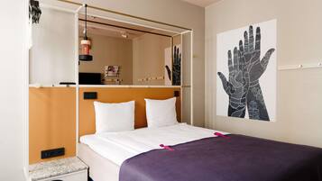 Una habitación de hotel con cama, mesita de noche, espejo y una obra de arte en la pared.