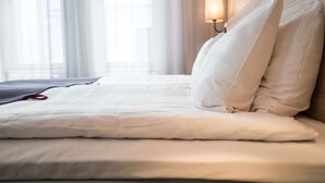Un letto rifatto con lenzuola e cuscini bianchi, una lampada da comodino e tende trasparenti in una camera d'albergo.