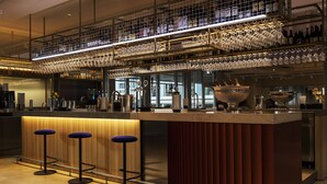 Zona bar moderna con bancone in legno, due sgabelli e vetrina per bicchieri sopra.
