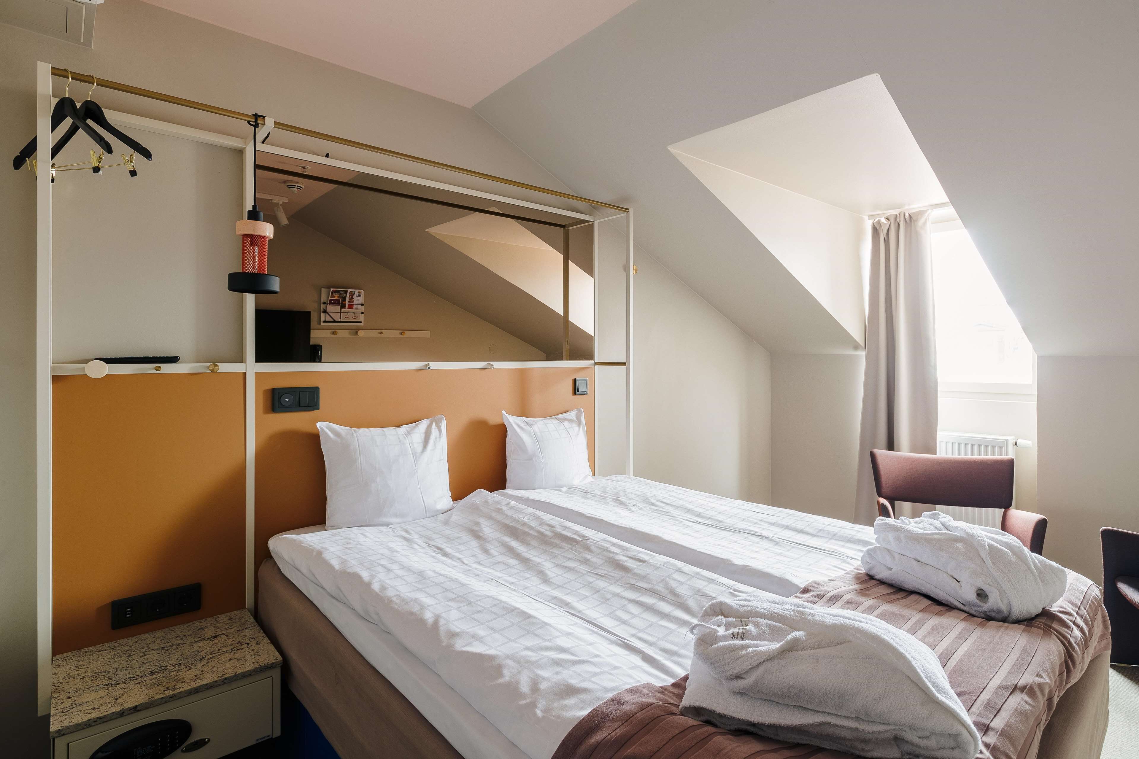 Una habitación de hotel con cama, una silla, un escritorio y un ventanal con cortinas.