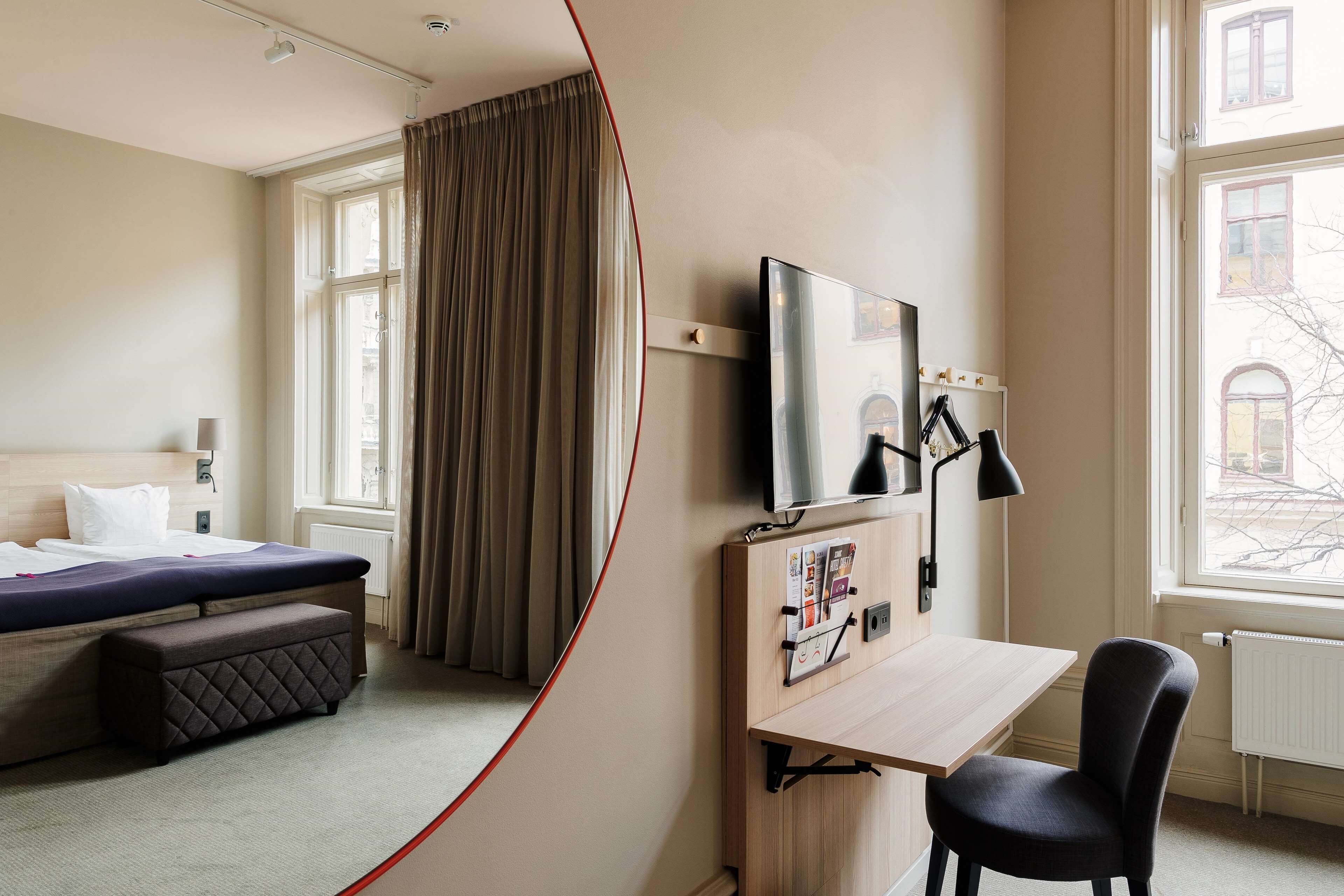 Habitación de hotel con cama, escritorio, silla, televisor y ventana con cortinas.