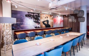 A modern restaurant with long wooden tables, blue chairs, and hanging pendant lights. - Scandic No 53 (Stockholm)