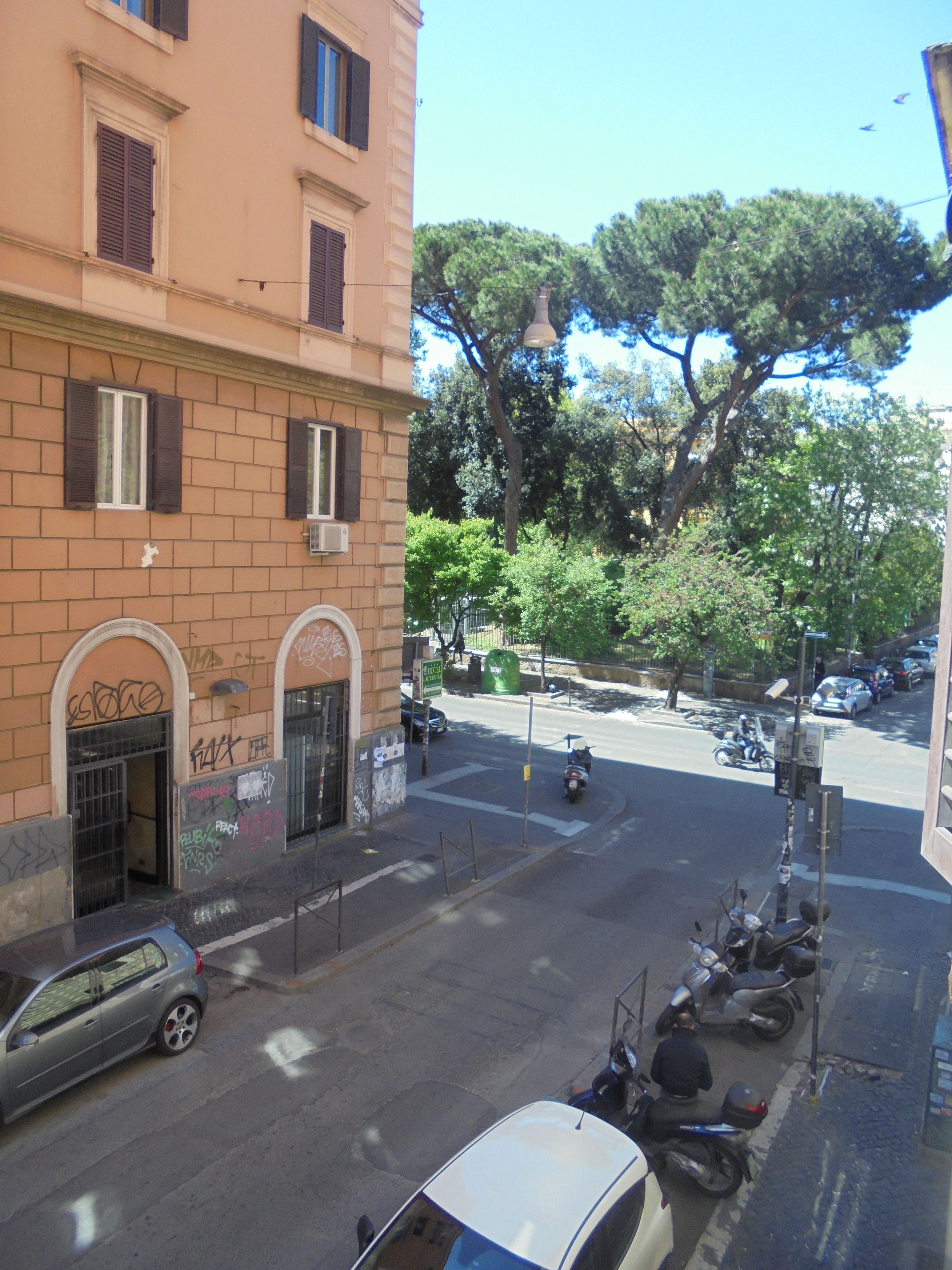 A street view with parked cars and a building with arched windows and graffiti.