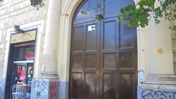 Facciata di un edificio con un'ampia porta ad arco, insegna di un caffè e graffiti sui muri.