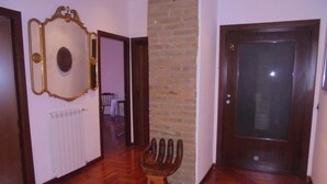 Un corridoio con pavimento in legno, una porta con un pannello di vetro e uno specchio appeso al muro.