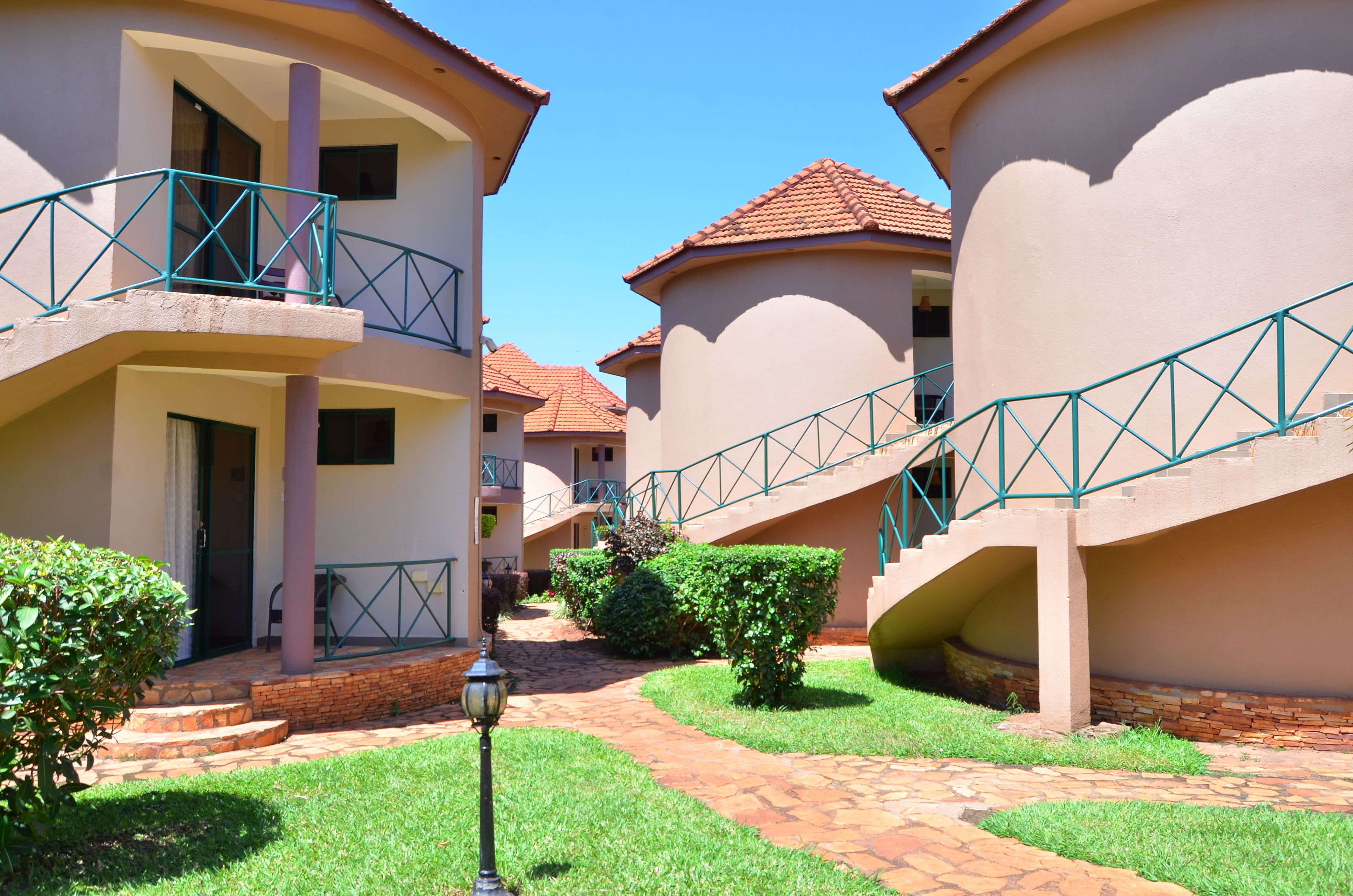 A courtyard with a brick pathway, a lamp post, and a staircase leading to a building with a balcony.